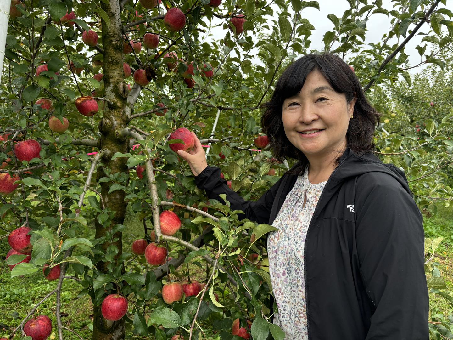 りんごの木の前で果実を手に微笑む女性(沼田)