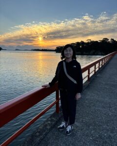 松島湾の赤い橋上で入江が朝焼けの海と雲を背に立つ記念写真。静かな水面と島影