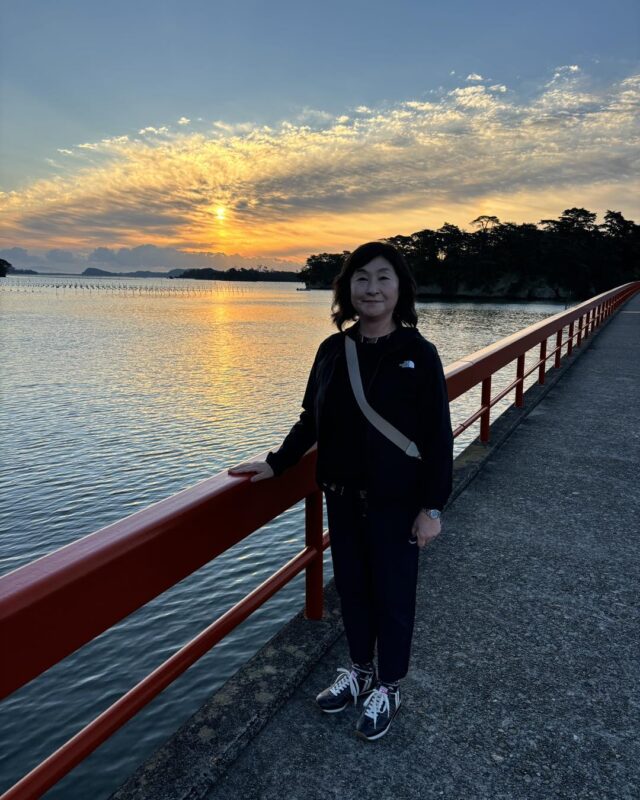 松島湾の赤い橋上で入江が朝焼けの海と雲を背に立つ記念写真。静かな水面と島影