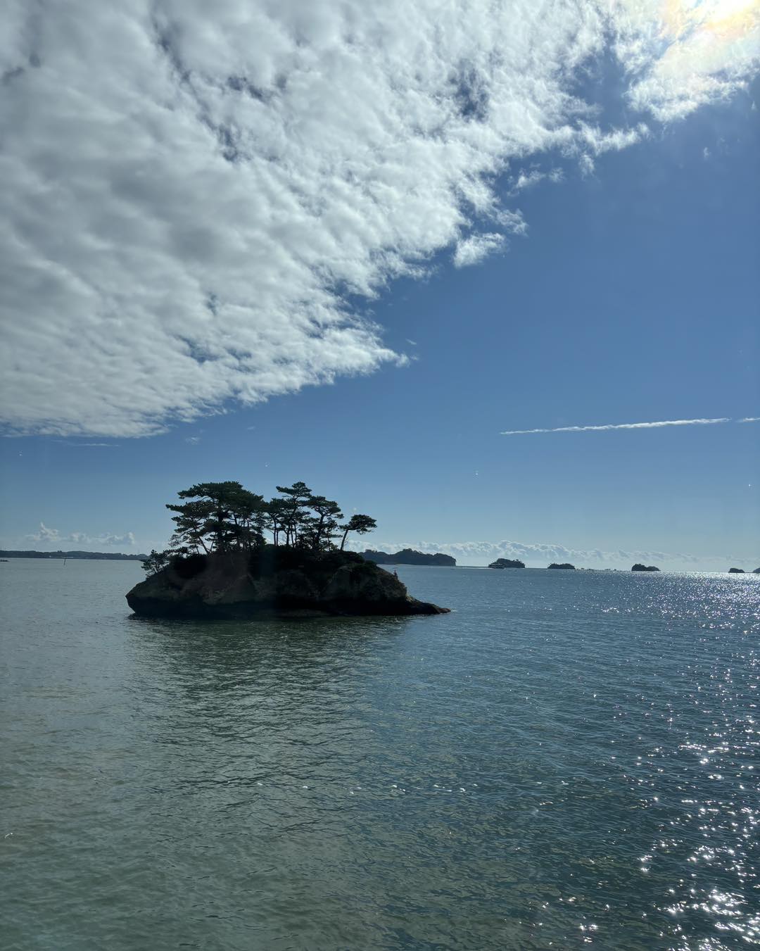 松島湾に浮かぶ小島と松を望む澄んだ海景。雲間からの陽光が水面に反射